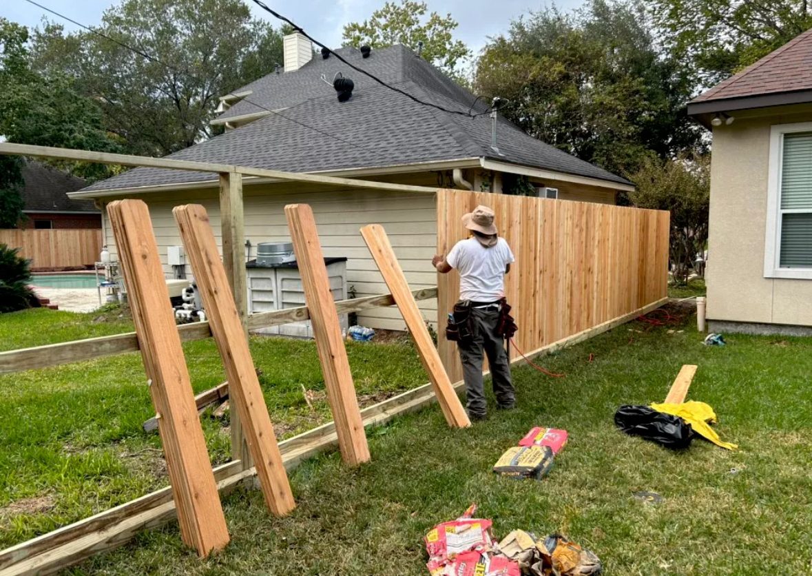 An L&K crew member building a cedar privacy fence in a Houston backyard